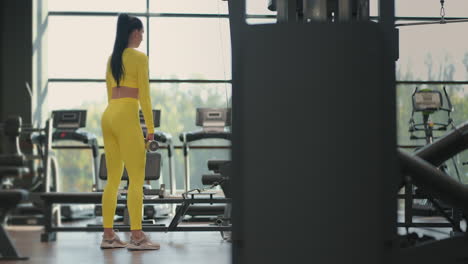 Fit-hispanic-woman-performing-weight-lifting-deadlift-exercise-with-dumbbell-at-gym-In-yellow-sportswear.-woman-brunette-fitness-performing-doing-deadlift-exercise-with-dumbbell
